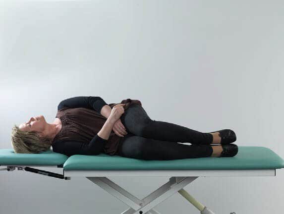 Female patient in black clothes lying on her right side on examination table. She has her head turned about 90 degrees toward the left.