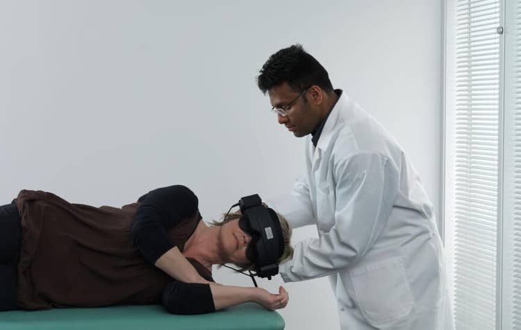 Male clinician rolling female patient onto her left. The patient is visibly wearing VNG goggles.