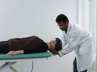 Clinician stood behind patient lying on their back on a green examination bed. The clinician is turning the patient’s head toward the left at a 45-degree angle.