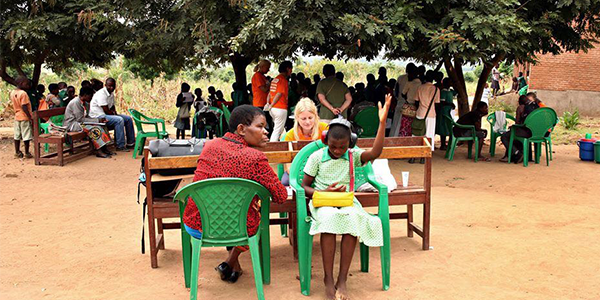 Rie Luxhoei peforming hearing screening in young girl, who is faced away from Rie and has her left arm raised