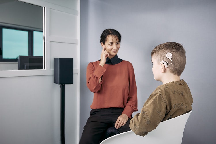 The clinician is pointing toward their ear to instruct the patient to listen for sounds.
