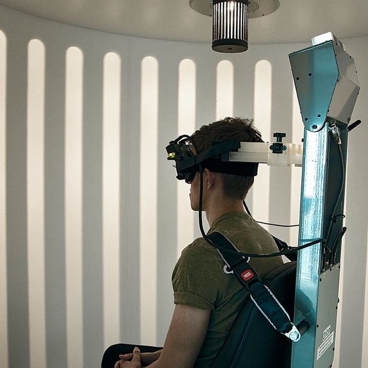 Patient strapped into the enclosed Orion Comprehensive chair and wearing VNG goggles. The light from the optokinetic drum above the patient is displaying a visual pattern across the wall of the booth enclosure.