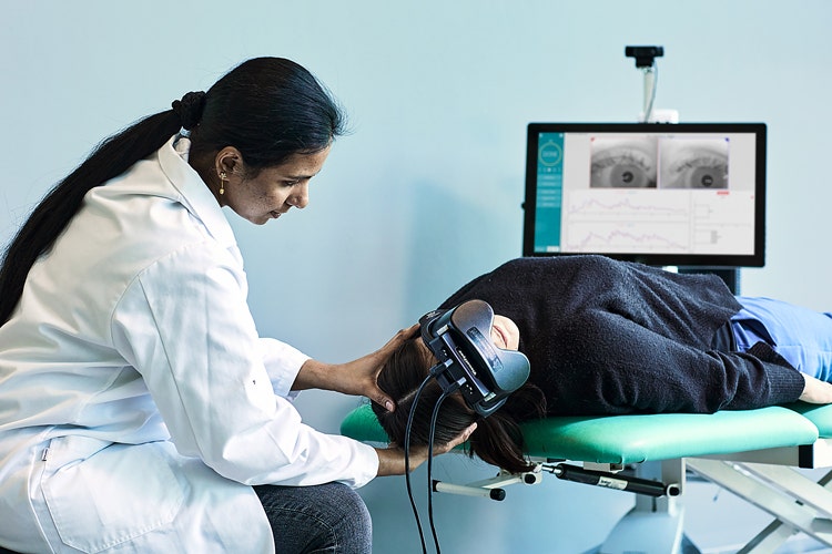 Clinician supporting the head and neck of a patient, who is laying supine on an examination bed with their head and neck hanging off the edge turned 45 degrees to their right.