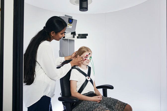 Young female patient sitting in Orion Auto-Traverse. Female clinician attaching electrodes to the patient's face.