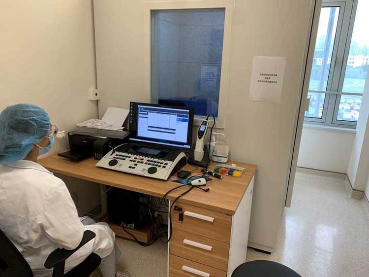 Female clinician sat at small desk with a printer, an Interacoustics audiometer, and the Interacoustics Titan.