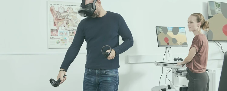 Patient wearing Vive Focus Vison VR headset performing ReflexVR module using controllers with a clinician observing