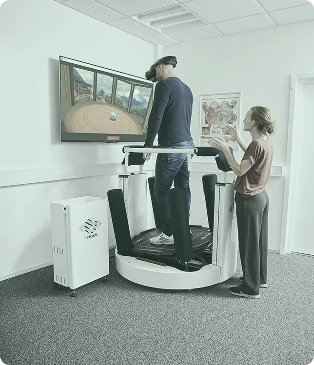Patient wearing Vive Focus Vison VR headset performing the Motion Program module while stood in the Virtualis MotionVR Computerized Dynamic Posturography (CDP) system. A clinician is stood behind ready to offer support if needed