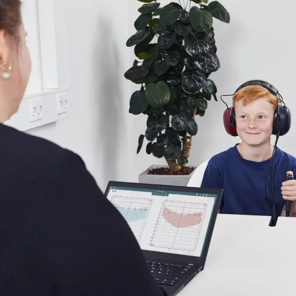 Boy wearing headphones for a hearing test while a clinician notes results on a tablet