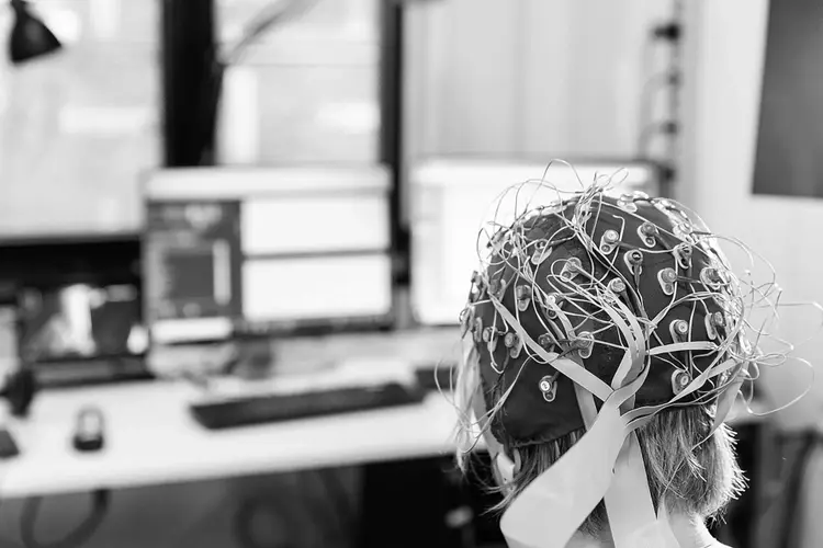 Research participant wearing an EEG electrode cap in front of audiological measurement screens