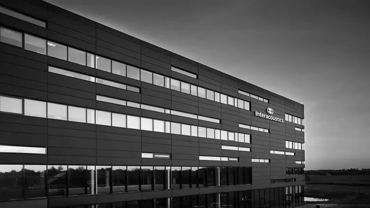 The Interacoustics headquarters building in Middelfart at dusk, with the Interacoustics logo on its facade