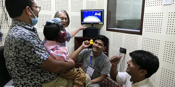 Clinicians demonstrating hearing screening equipment to a family in a Nepal clinic