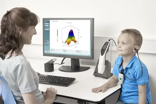 A clinician tests a boy's middle ear with the handheld Titan beside a computer screen