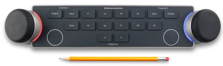Audiometer Keyboard seen from above with a pencil below. For size comparison, the pencil is approximately two thirds the width of the keyboard. There are two dials located on the left and right sides of the keyboard. The dials are encircled by LED lights which indicate different functions when in use. There are several keys between the multi-functional dials, which include and are not limited to input and output for channels one and two, store, two keys to decrease or increase the intensity, and nine F-keys labeled F1 to F9.